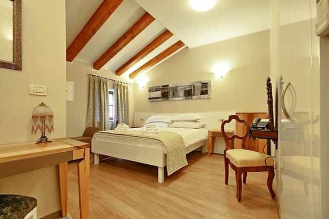 Hotel room with a double bed, wooden ceiling beams, desk, and chair.