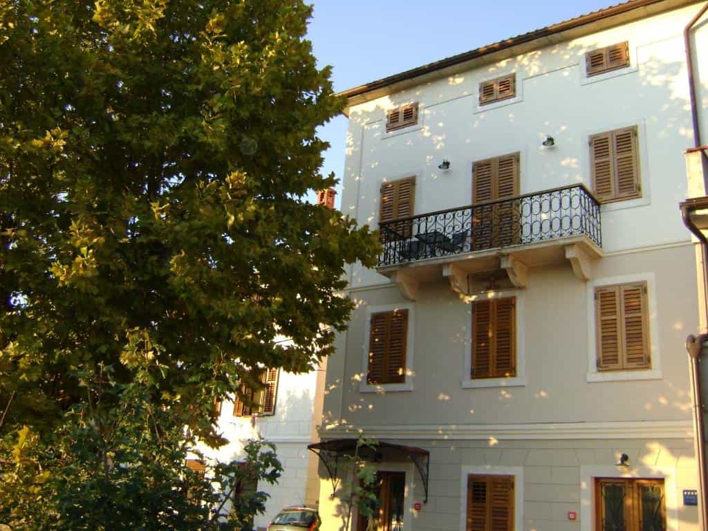 Multi-story building with brown shutters and a wrought-iron balcony next to a large tree.
