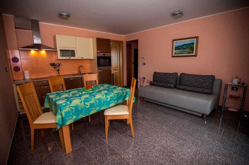 Open plan kitchen and living area with dining table, chairs, and sofa in a furnished apartment.