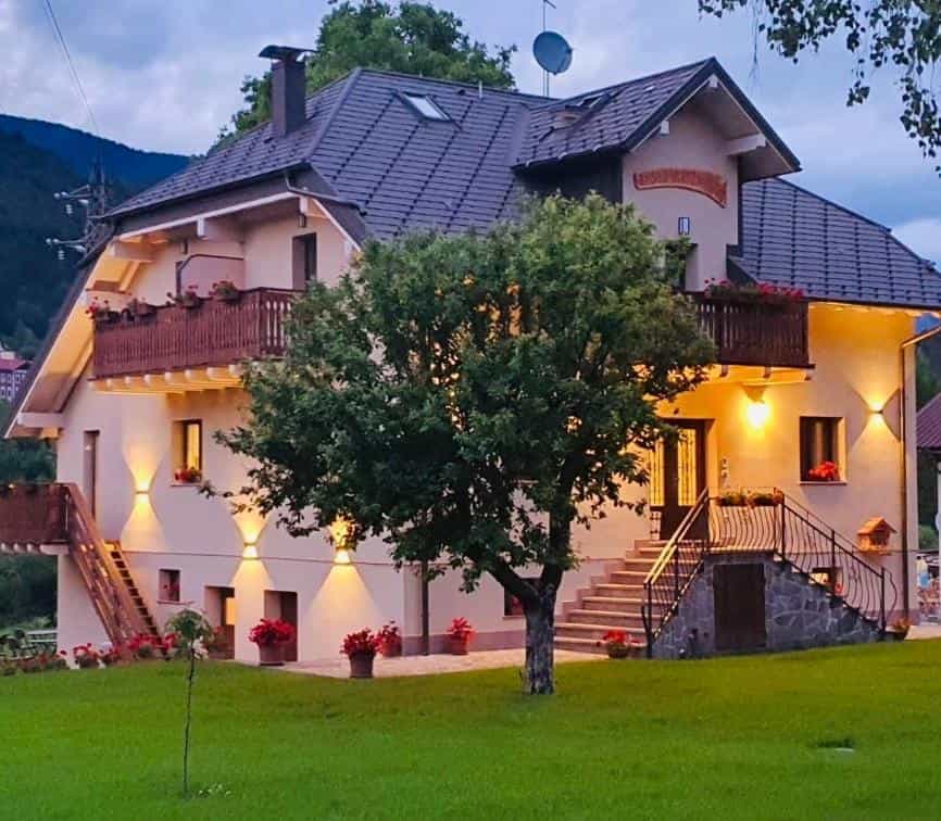 Two-story house with balconies, flower boxes, and outdoor lighting in a mountain setting.