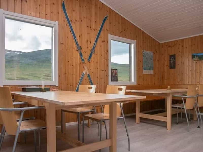 Wooden interior of Alesjaure hut with dining tables, chairs, and vintage skis mounted on the wall.