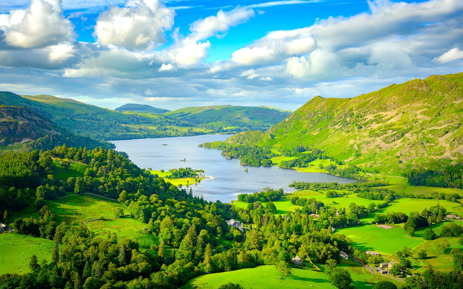 Lake surrounded by lush green mountains under a bright blue sky with white clouds in England.
