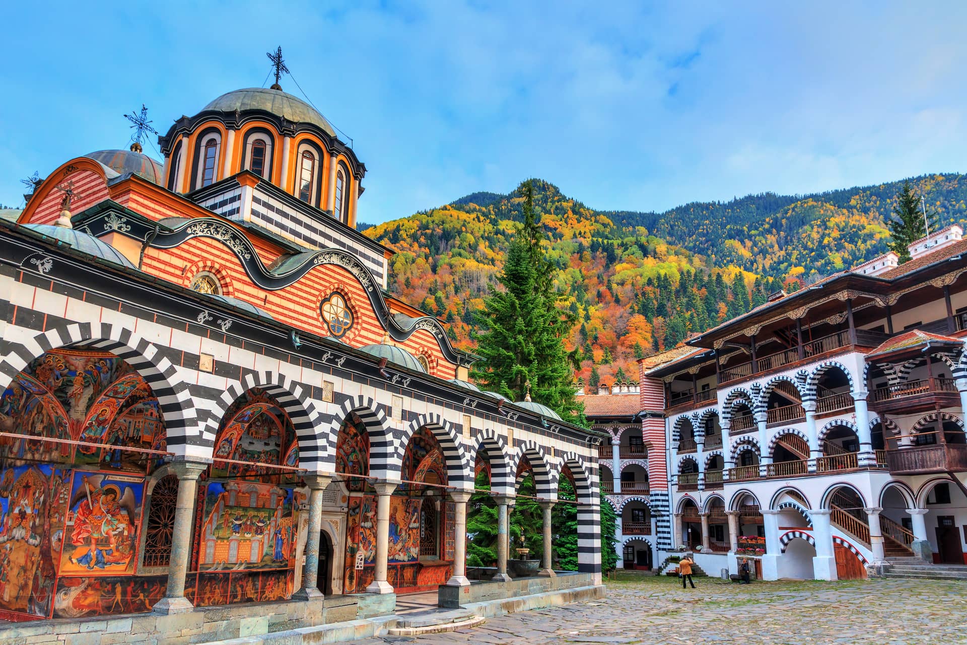 Rila Monastery with colorful frescoes and autumn foliage on mountain backdrop, Bulgaria.