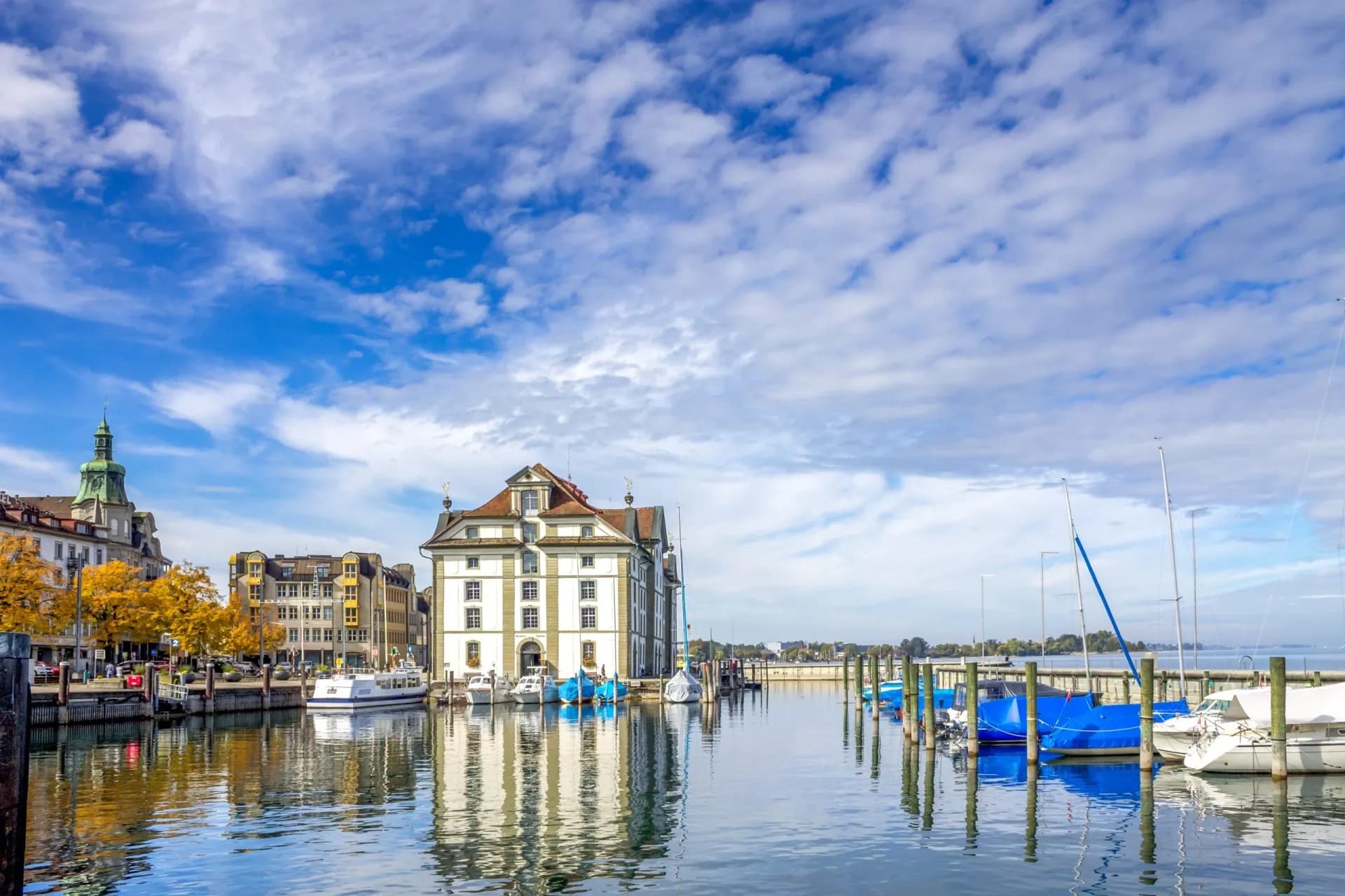 Boats docked in harbor next to historic buildings under a blue cloudy sky in Rorschach.