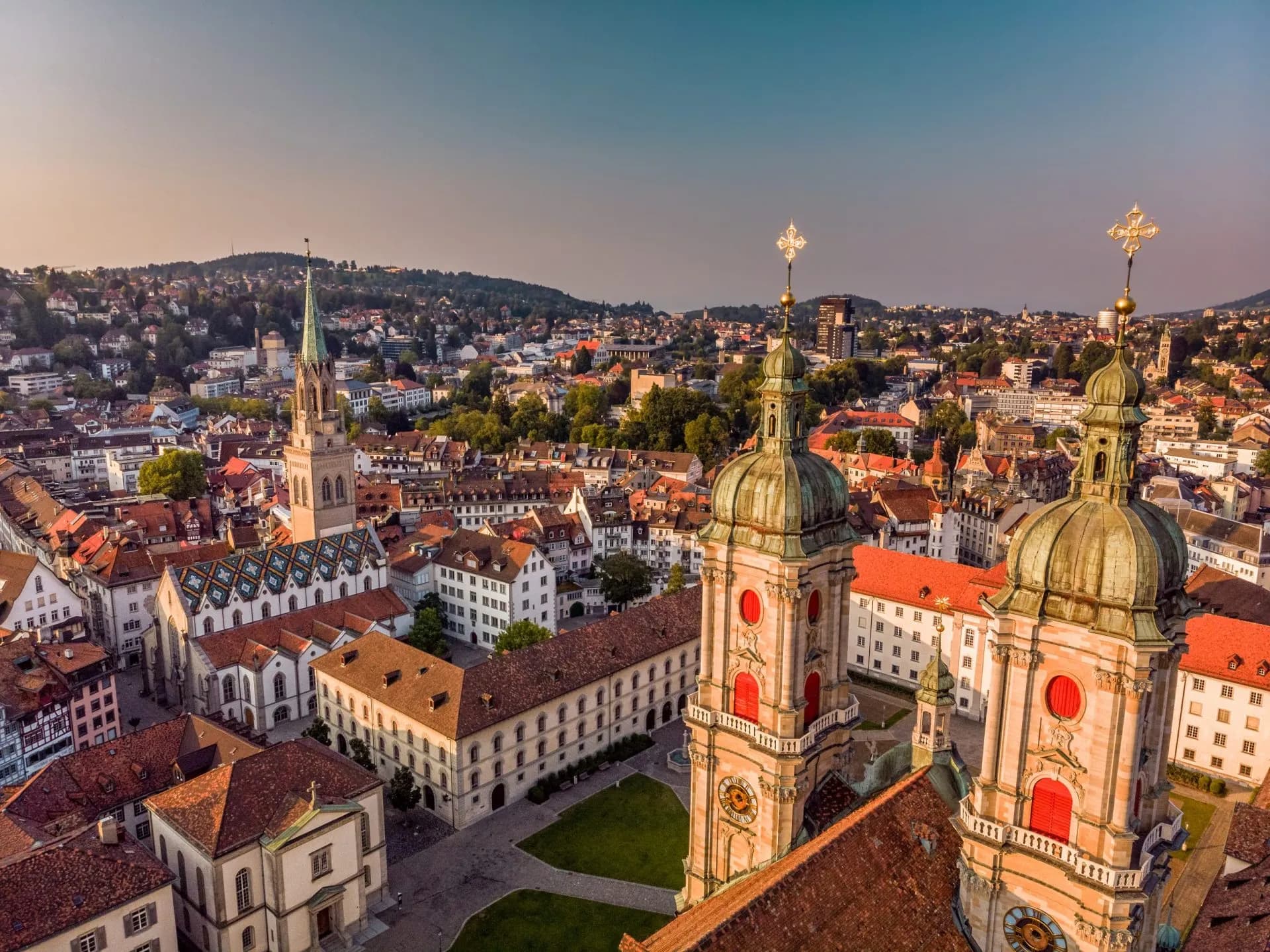 Aerial view of St. Gallen Abbey and Monastery towers overlooking historic city and green hills.