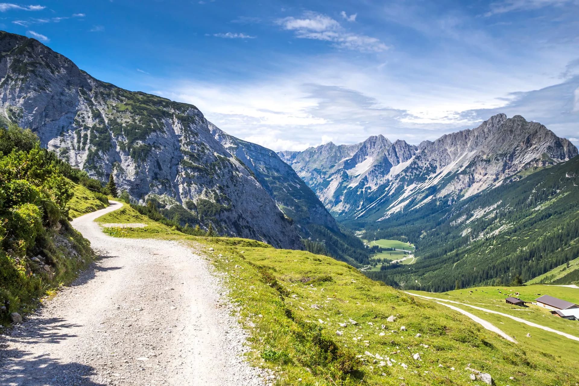 Winding gravel path above green alpine valley leading toward jagged Karwendel mountains