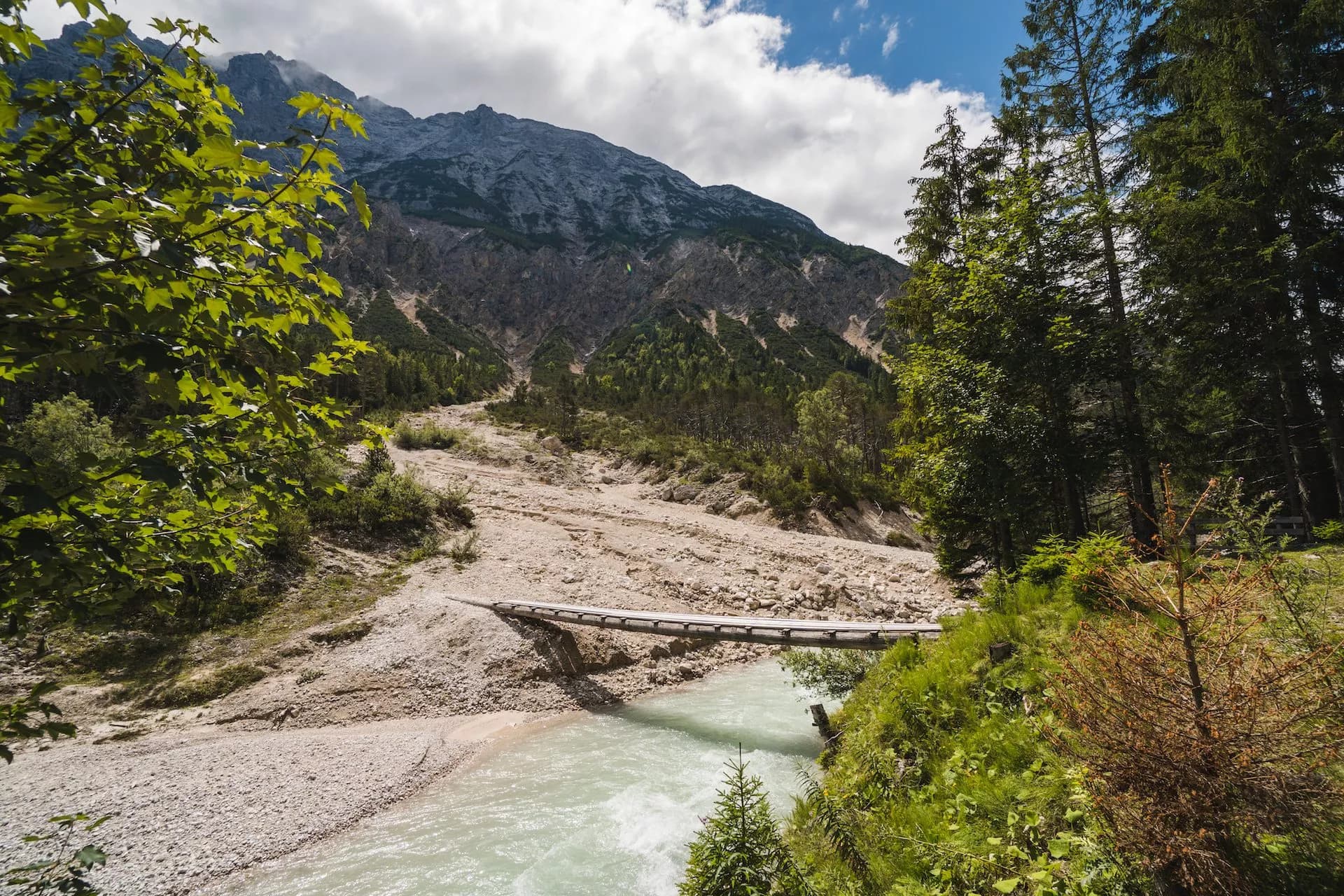 Wooden bridge over milky river flowing through rocky valley below Karwendel mountains.