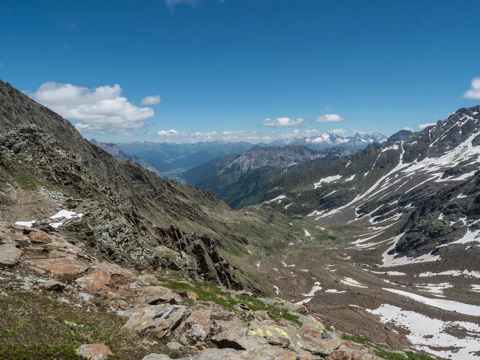 Rocky mountain valley with patches of snow under a bright blue sky.