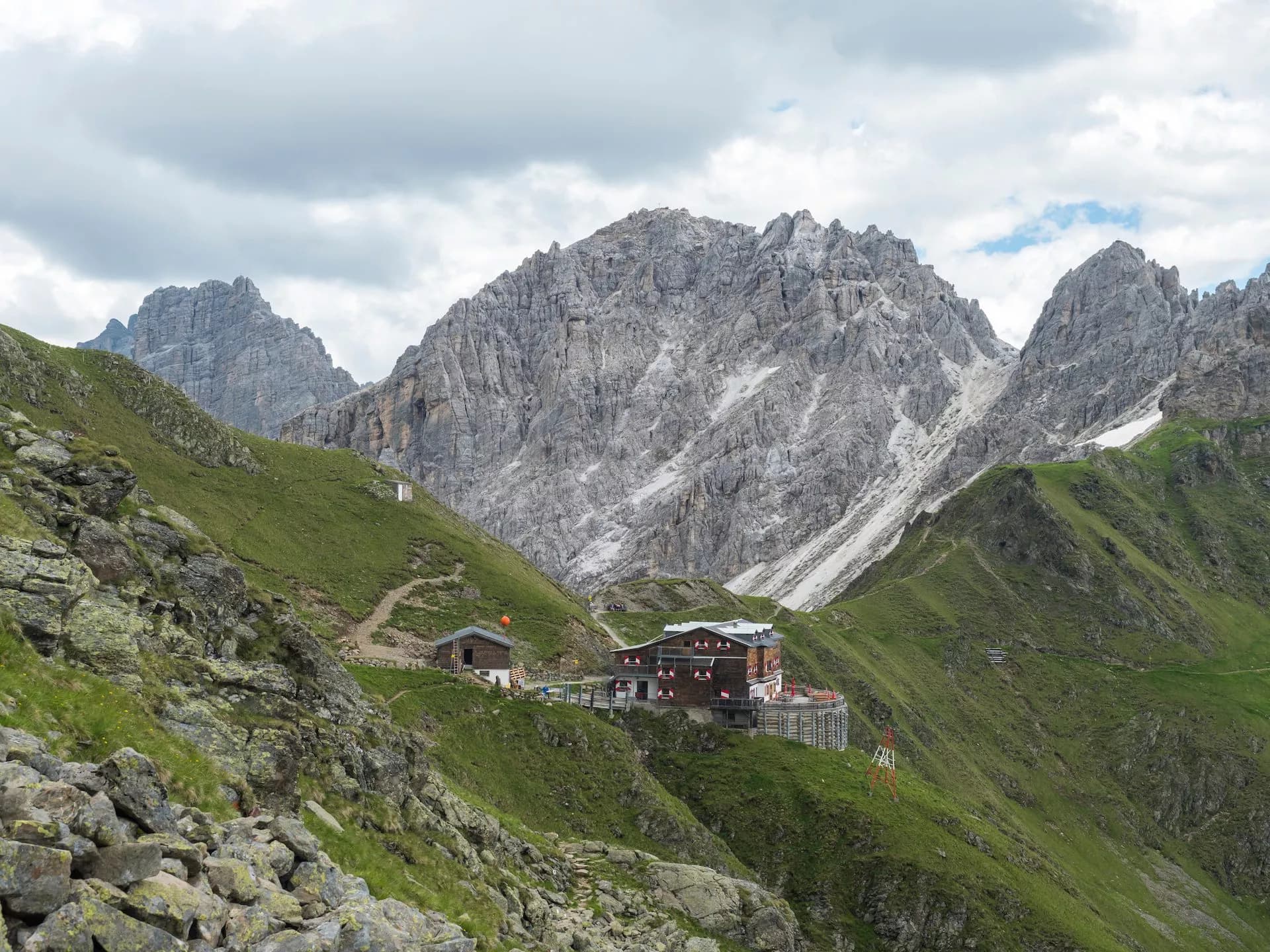 Innsbrucker Hutte mountain refuge nestled in green alpine slopes below rocky peaks under cloudy sky.