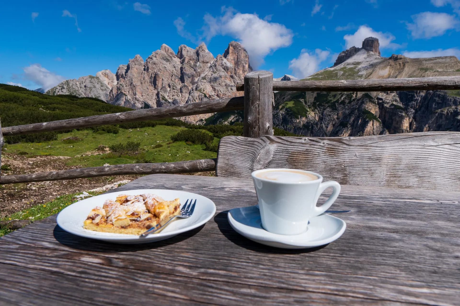 Coffee and pastry break on rustic wooden table with mountain view and blue sky