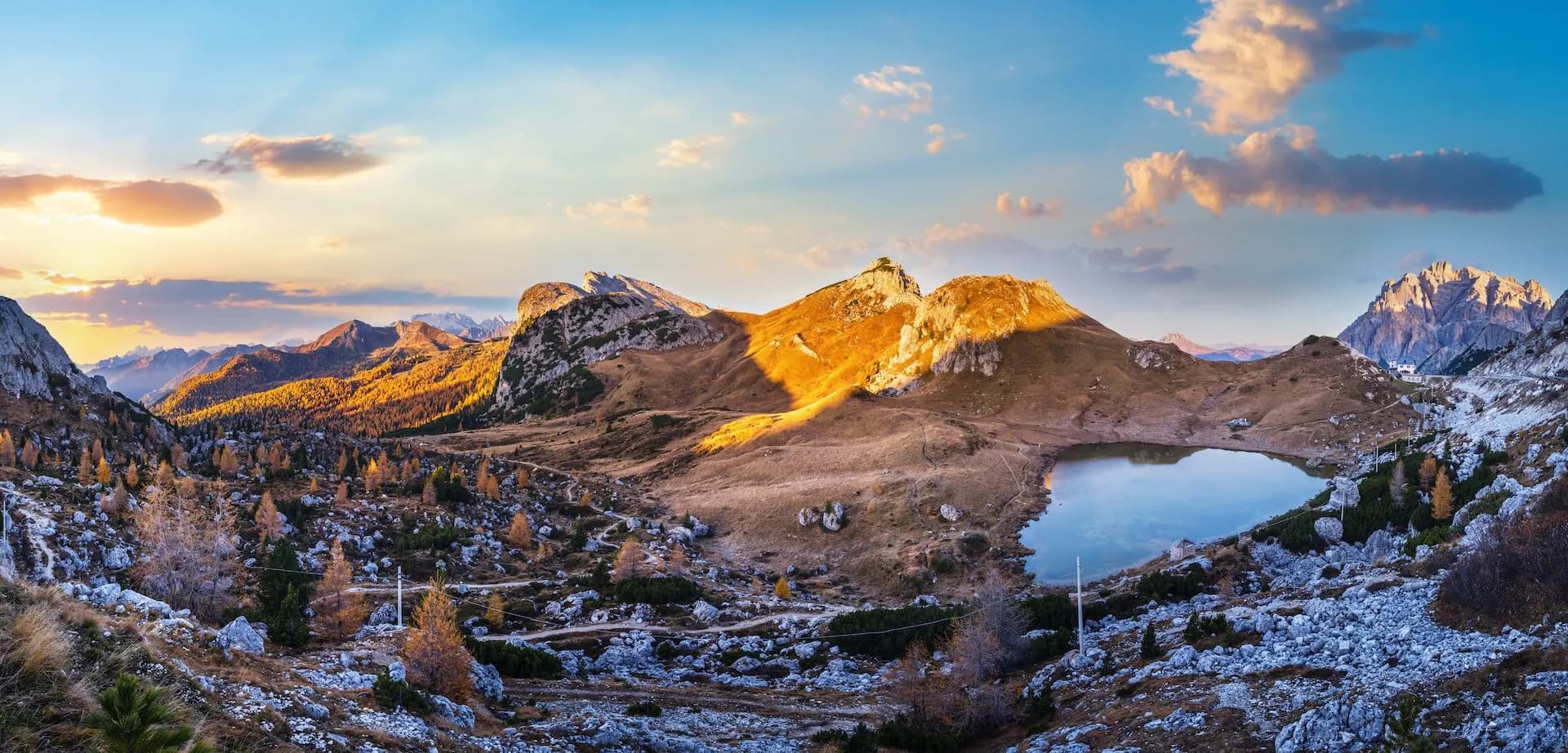 Alpine lake reflecting mountains at sunset with autumn foliage and rocky terrain, Valparola Lake.