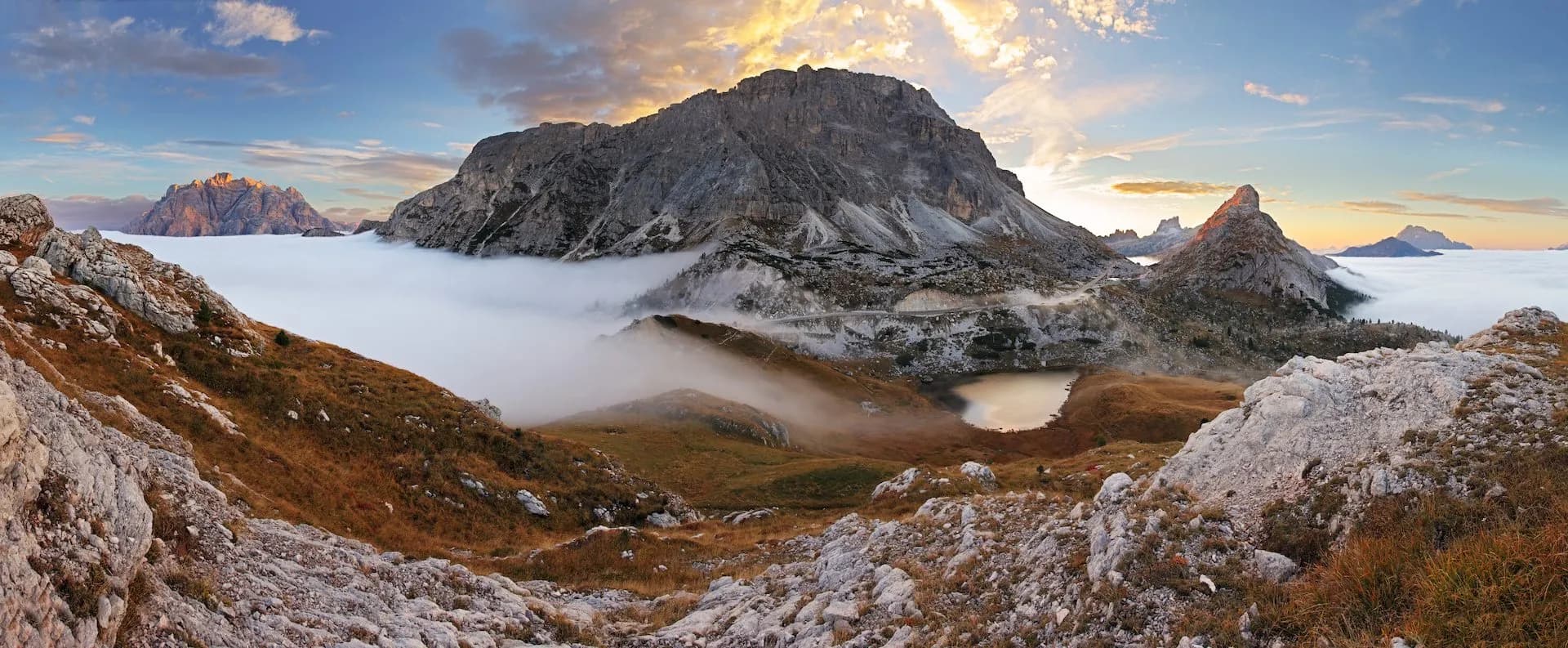 Mountain landscape above fog inversion at Valparola Pass with rocky foreground and sunset sky.