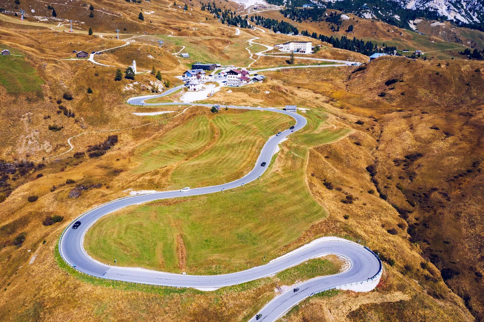 Winding mountain road with cars and motorcycles ascending grassy slopes near Passo Gardena.