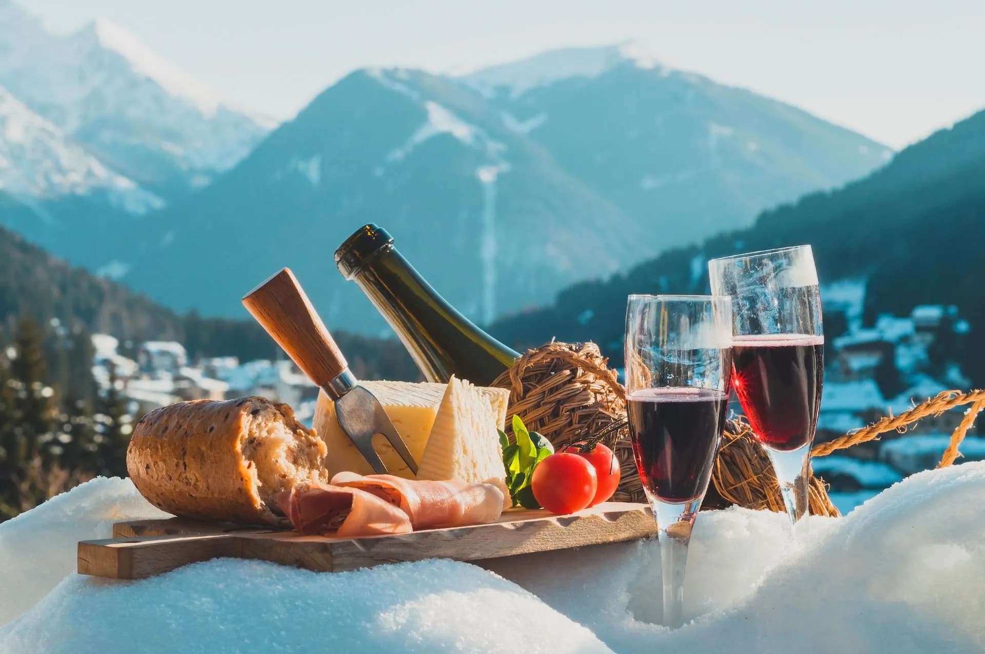 Winter picnic with cheese, bread, wine, and mountains in the Dolomites background.