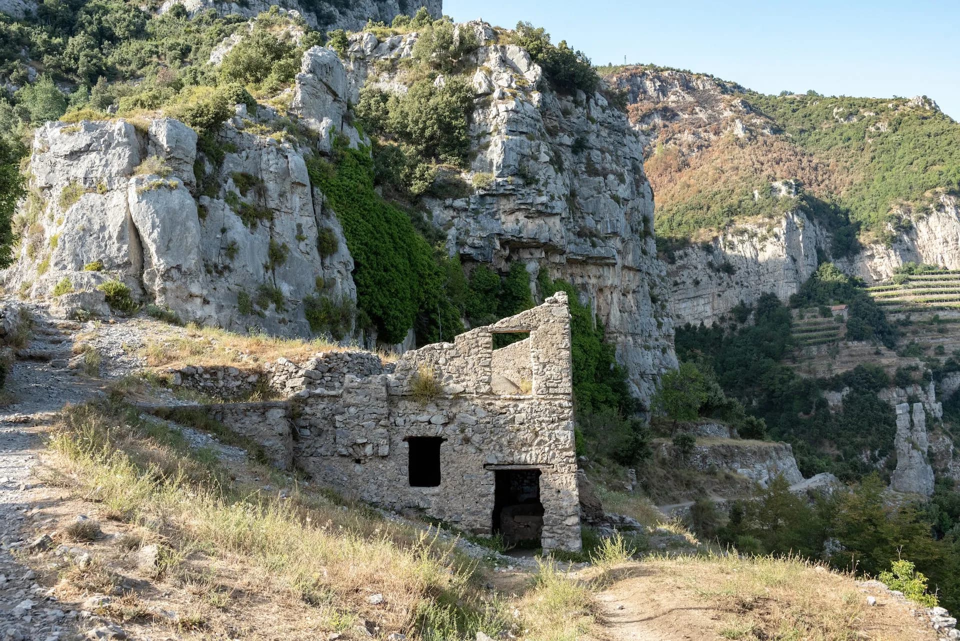 Hiking path above Positano with ruins against steep, rocky, green Mediterranean cliffs.
