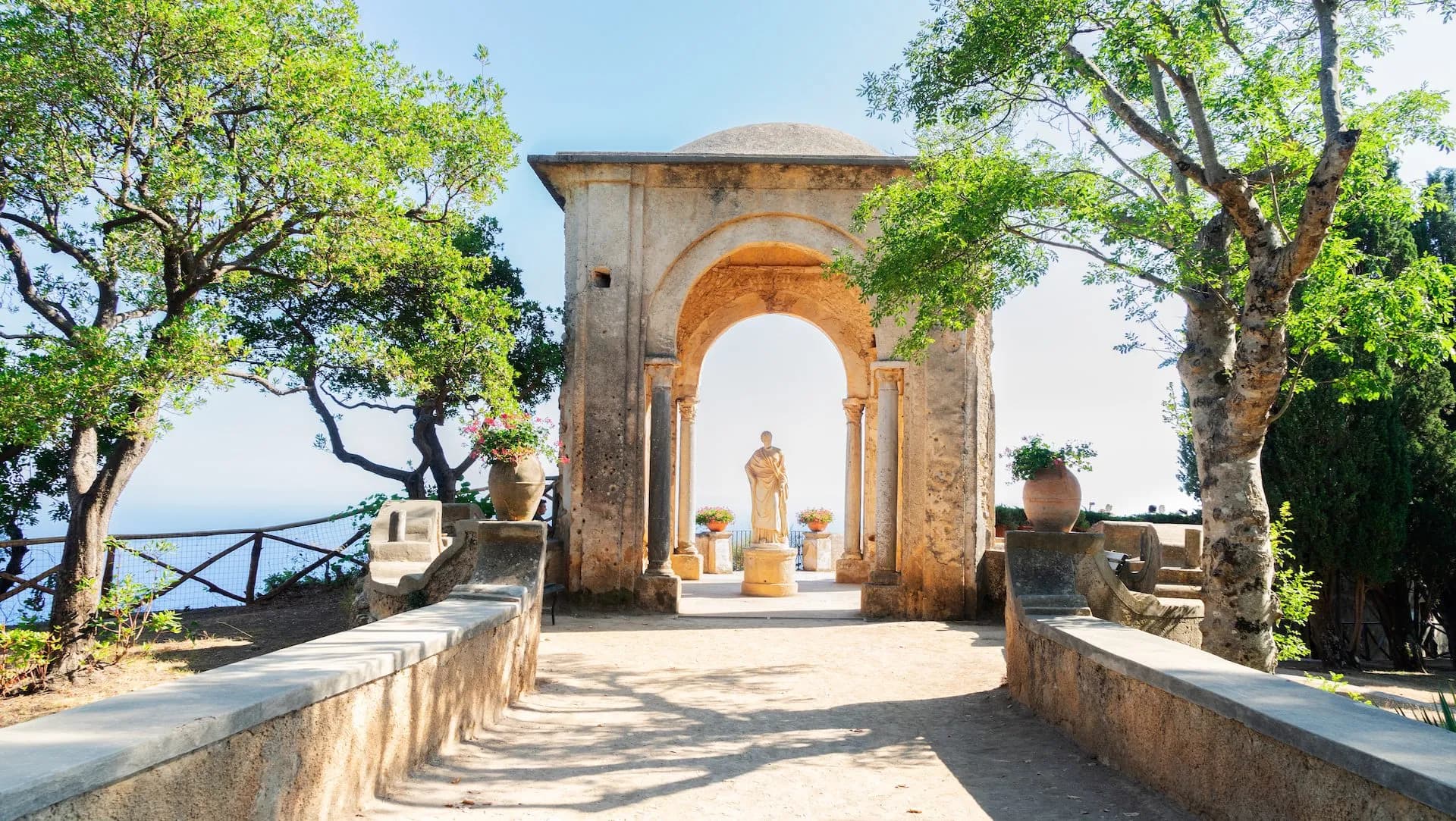 Stone archway leading to a statue overlooking the Mediterranean coastline in Ravello gardens.
