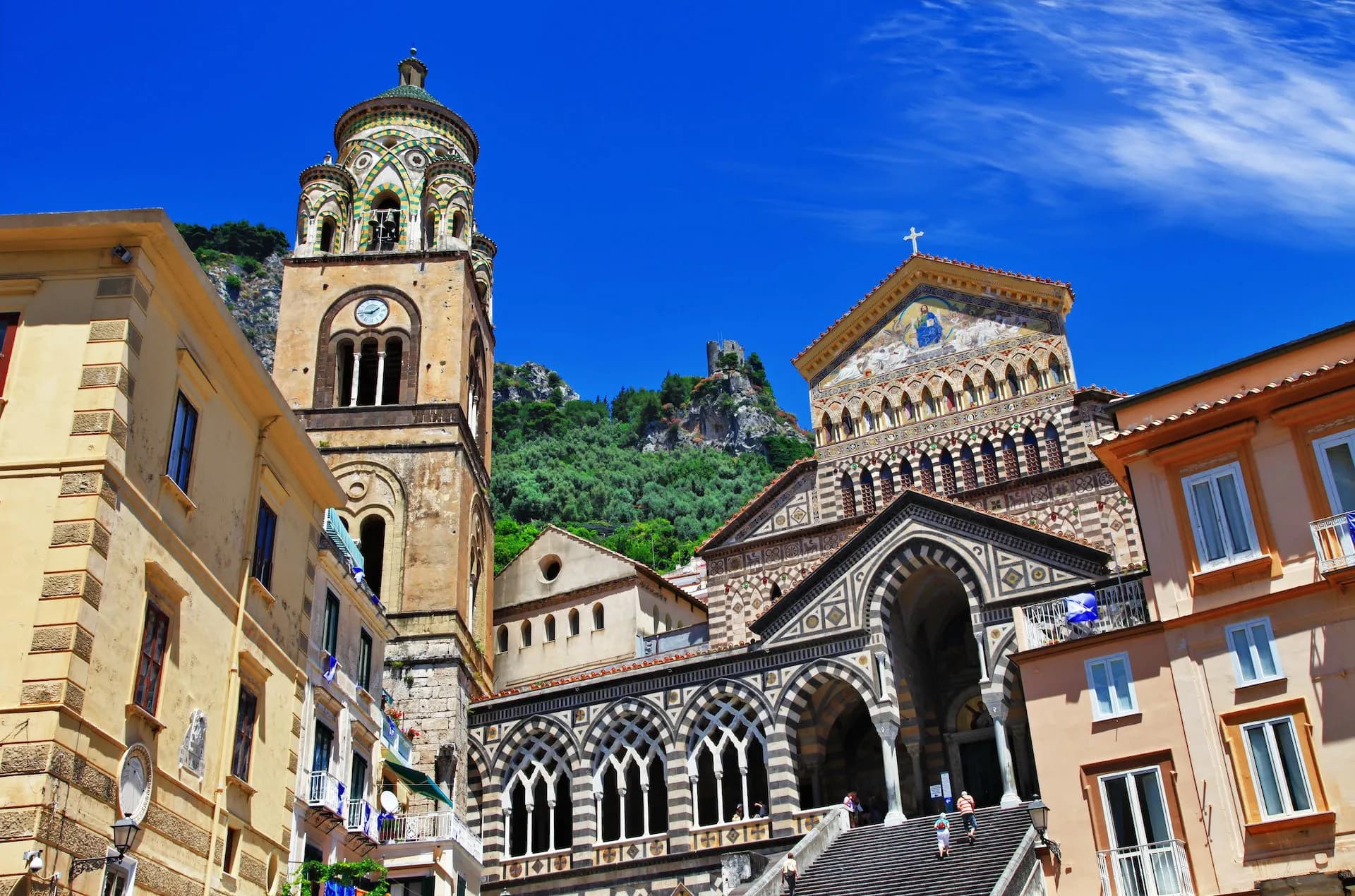 Cathedral of St. Andrea bell tower and ornate facade in Amalfi under a bright blue sky.