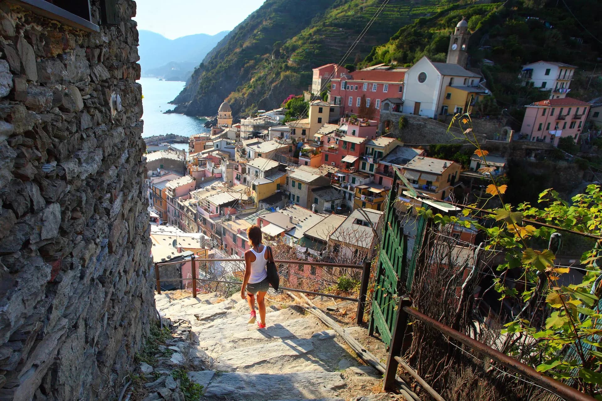 Woman walking down stone steps overlooking colorful houses of Vernazza on the Mediterranean coast.