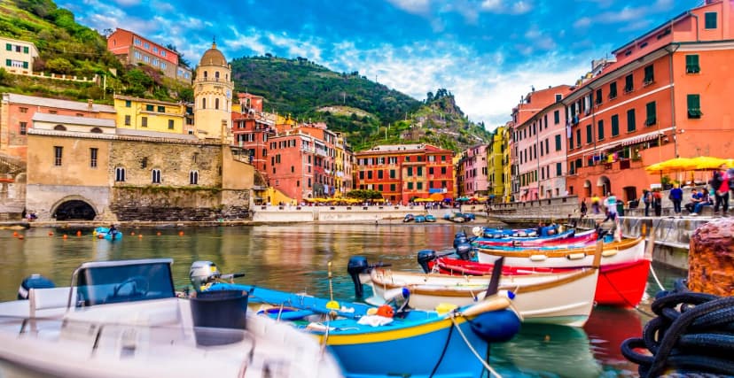 Colorful boats moored in harbor before hillside town with colorful buildings and church tower, Vernazza.