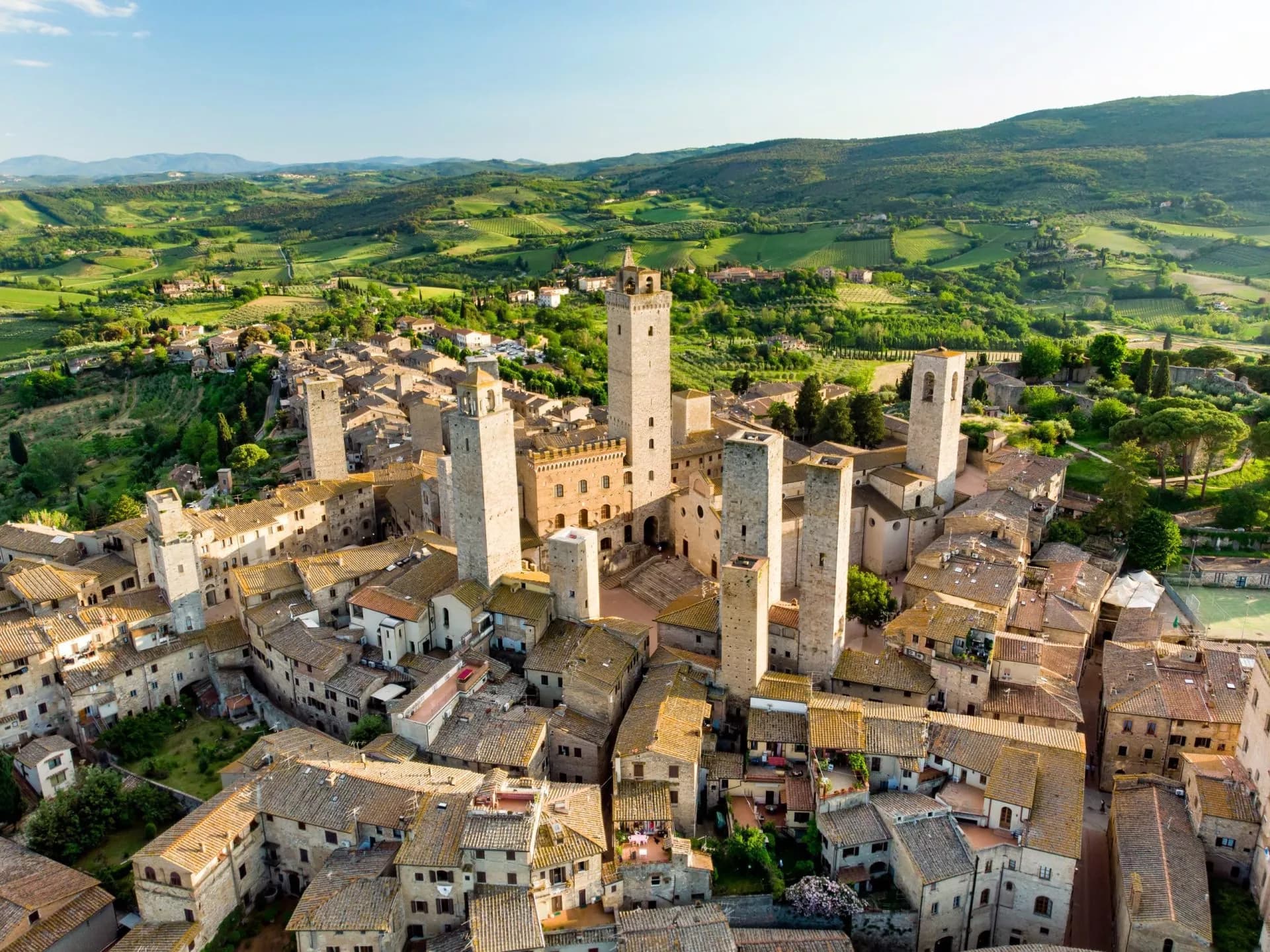 San Gimignano medieval towers above terracotta roofs surrounded by green Tuscan hills.