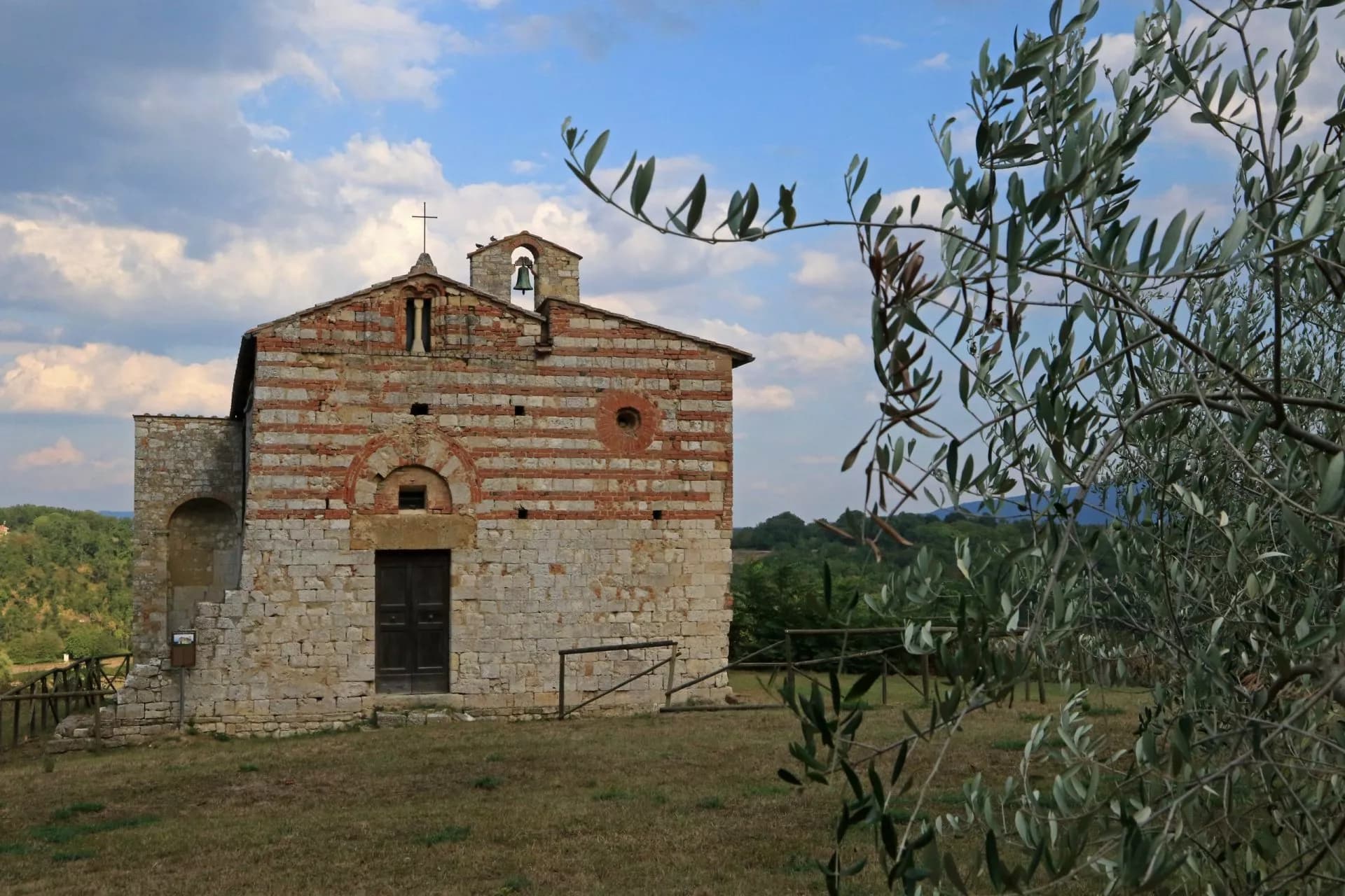 Stone church with red brick banding, olive branches in foreground, Pieve a Elsa.
