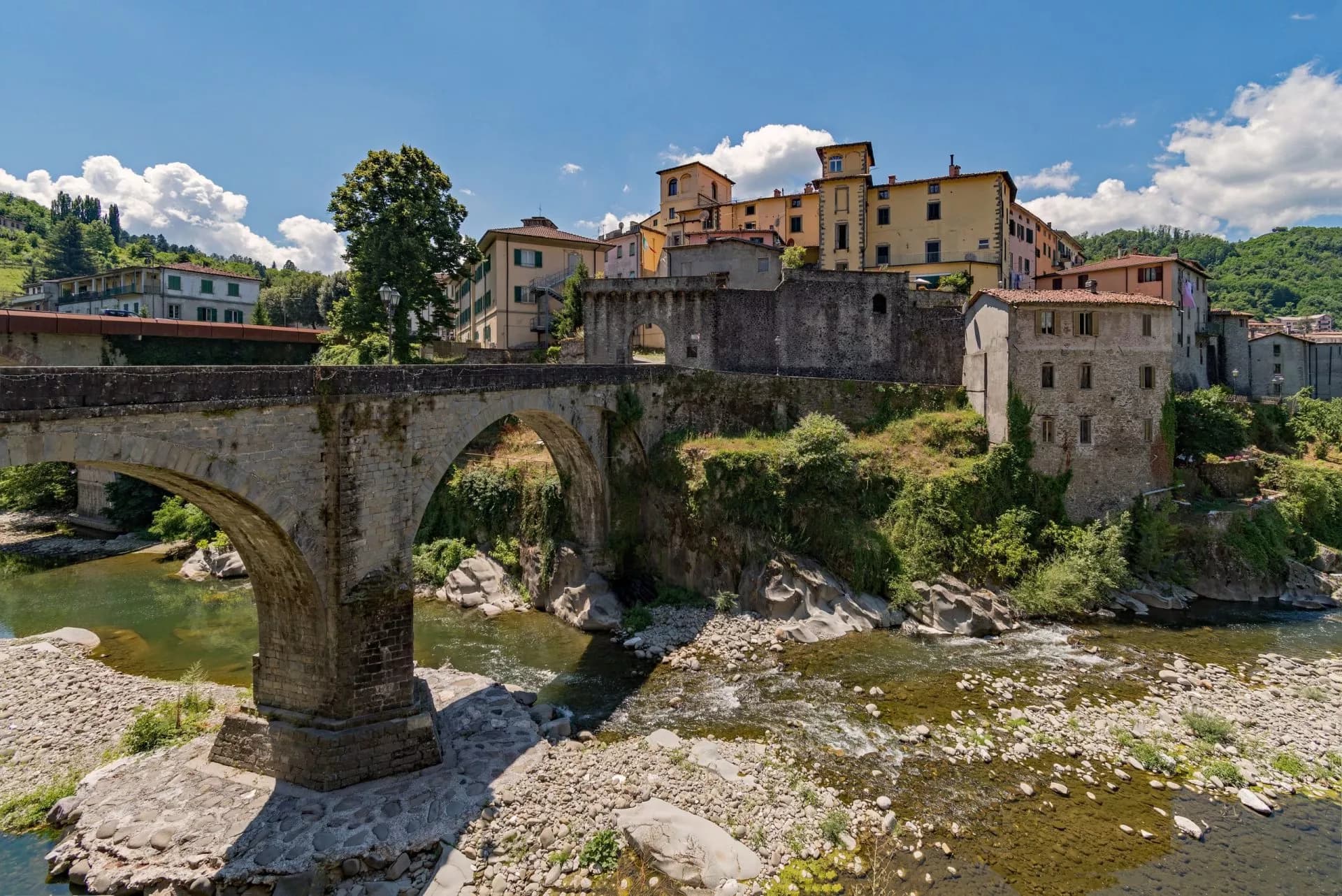 Stone arch bridge over a rocky river leading to historic buildings in Castelnuovo di Garfagnana.