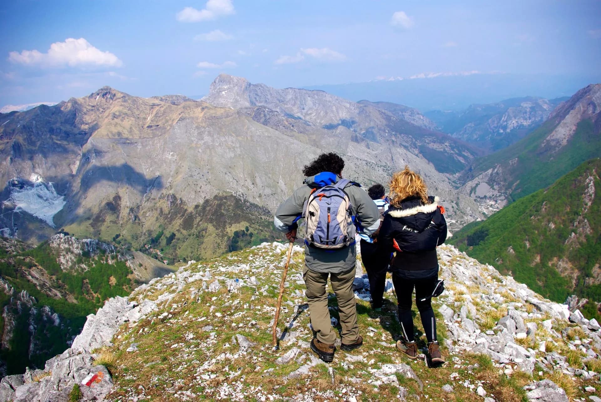 Hikers on rocky ridge overlooking vast, rugged mountains in the Apuan Alps.