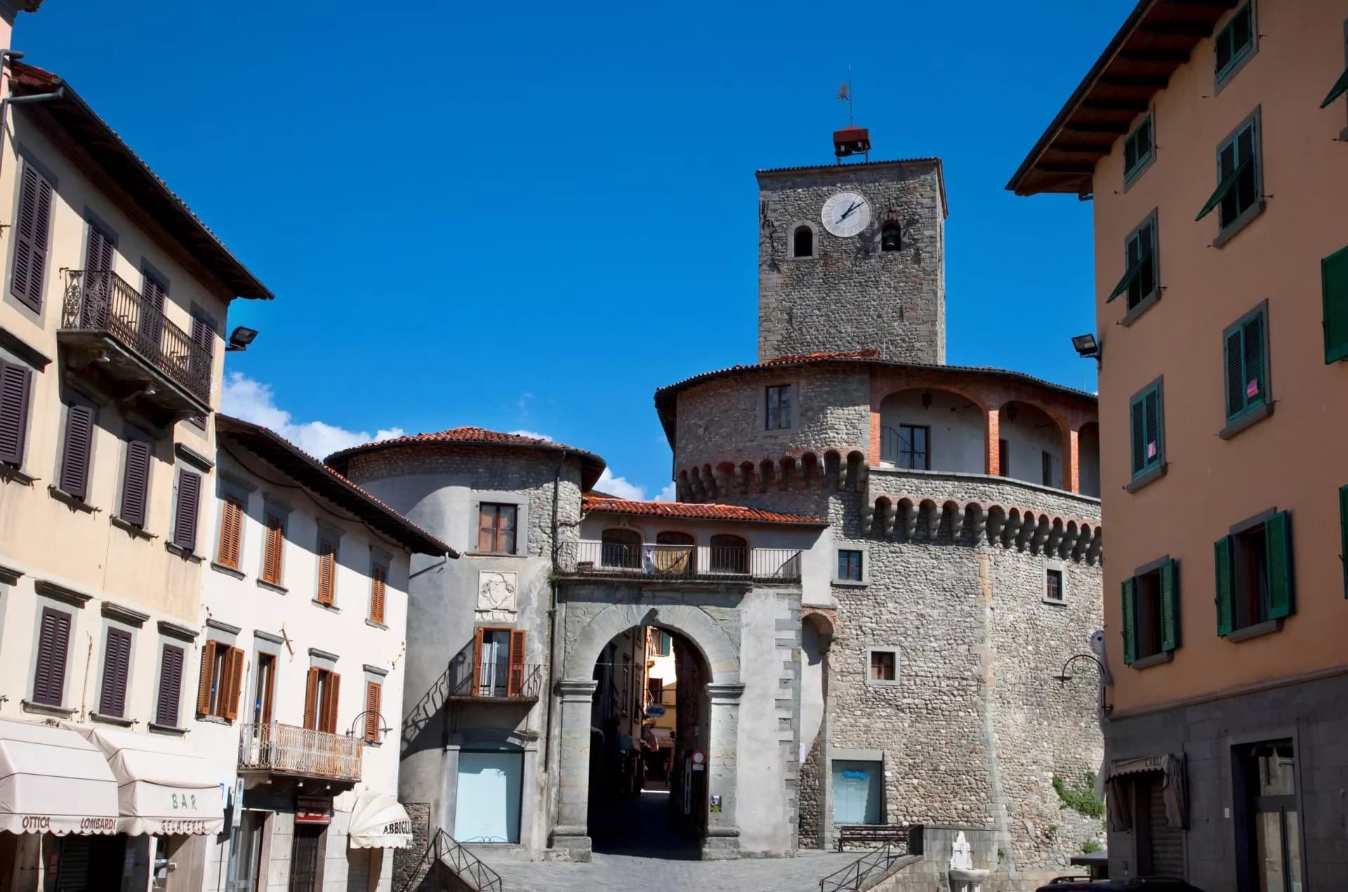 Clock tower and stone archway in Castelnuovo town square with surrounding historic buildings.