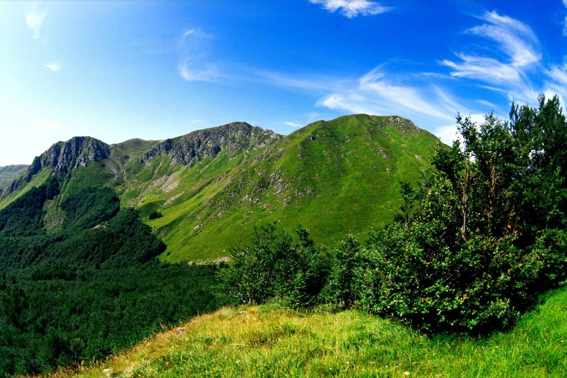 Green mountainsides under a bright blue sky with wispy white clouds, Monte Prado.