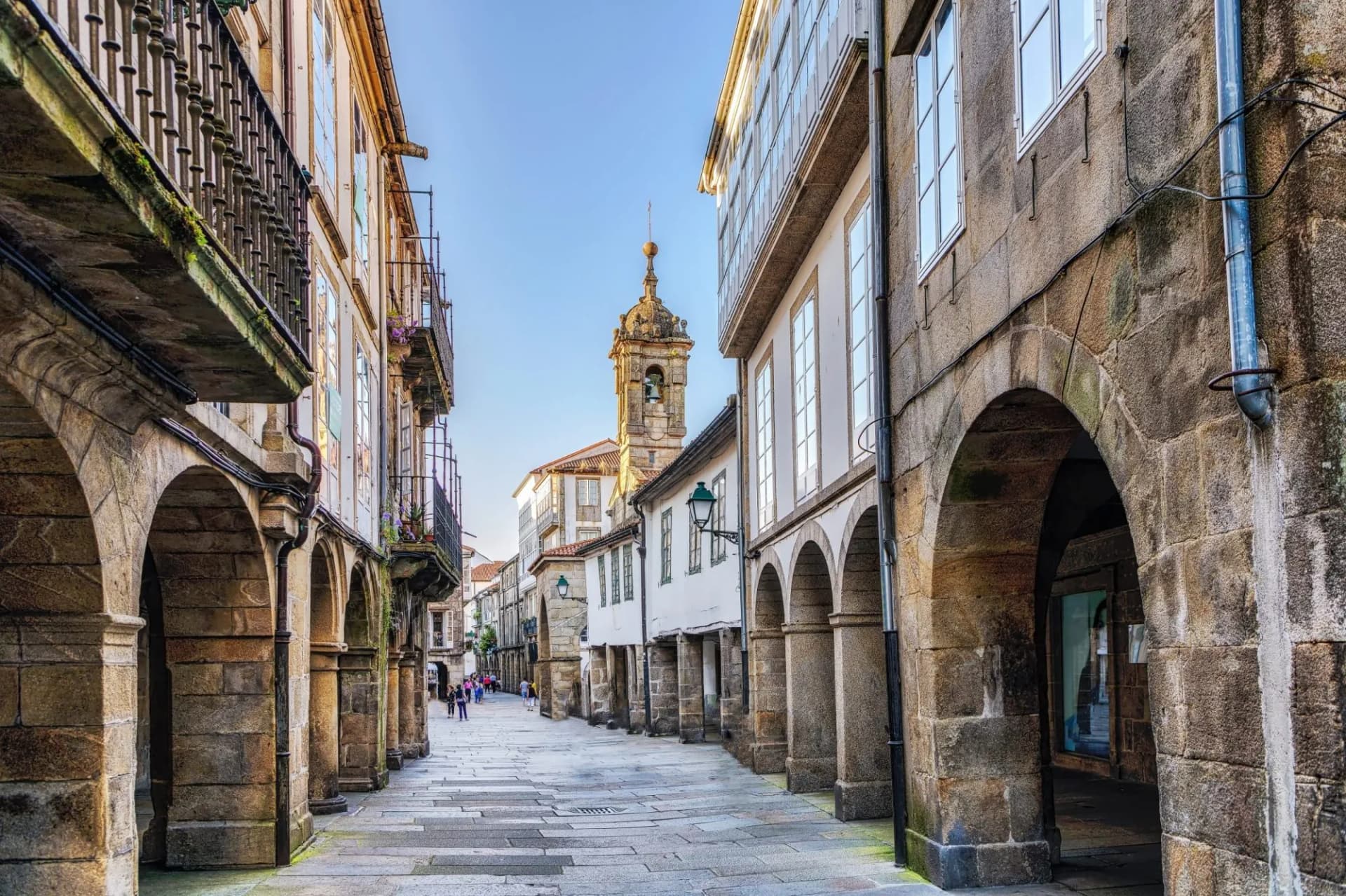 Narrow stone street with arcades leading toward a bell tower in Santiago de Compostela.