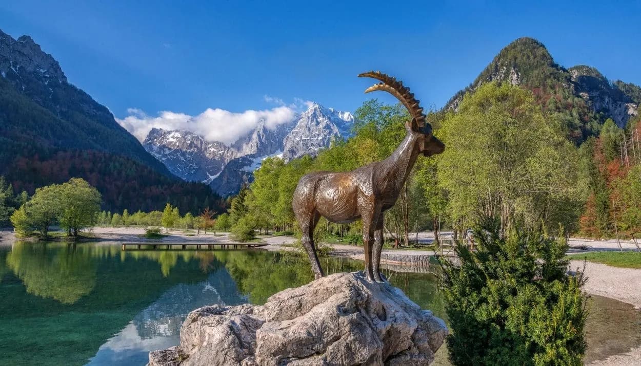 Bronze ibex statue by alpine lake with snow-capped mountains near Kranjska Gora