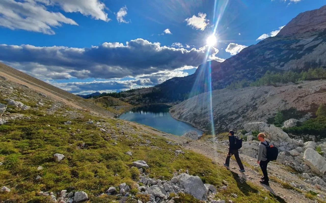 Hikers with backpacks walking near an alpine lake under bright sun and blue sky, Triglav Lakes.