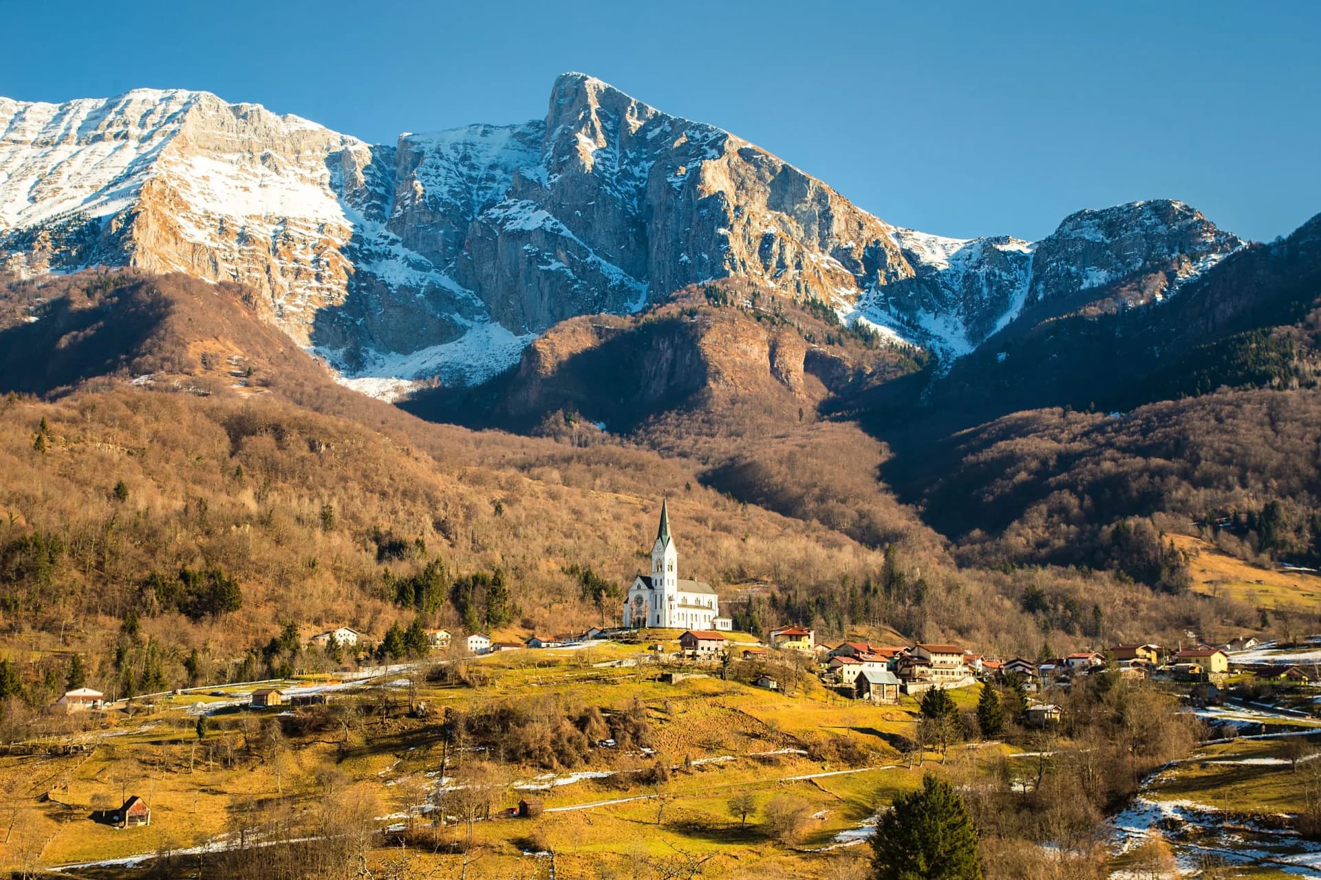 White church overlooking village nestled in valley below snow-capped mountains in Drezniča.
