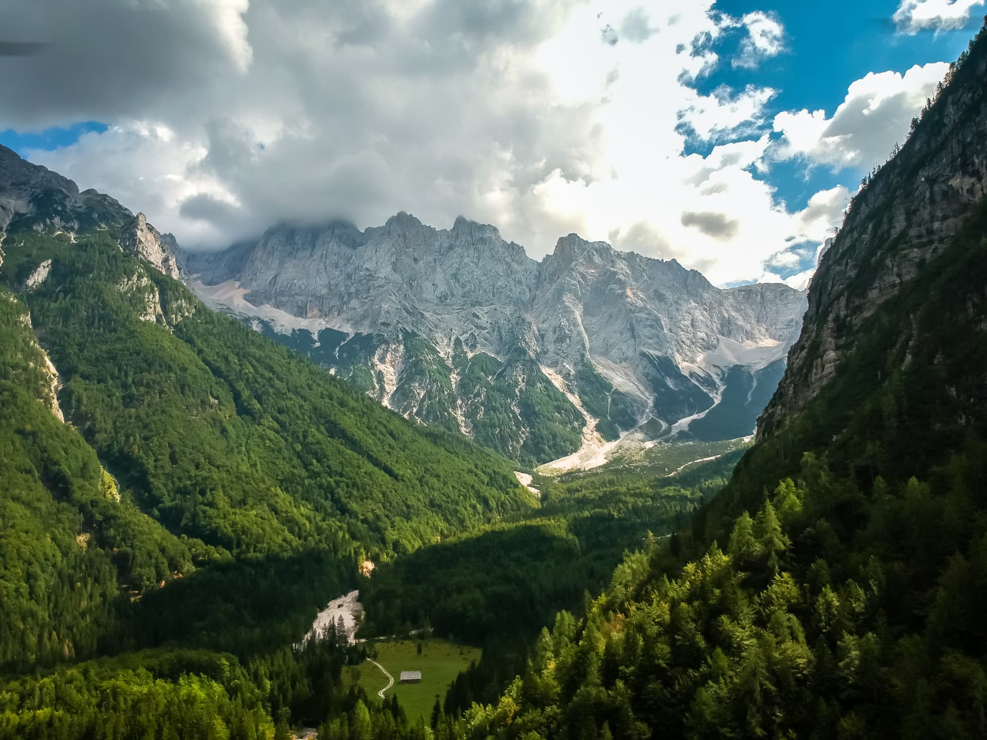 Alpine valley with steep forested slopes, rocky peaks, and a riverbed under dramatic clouds in Kranjska Gora.