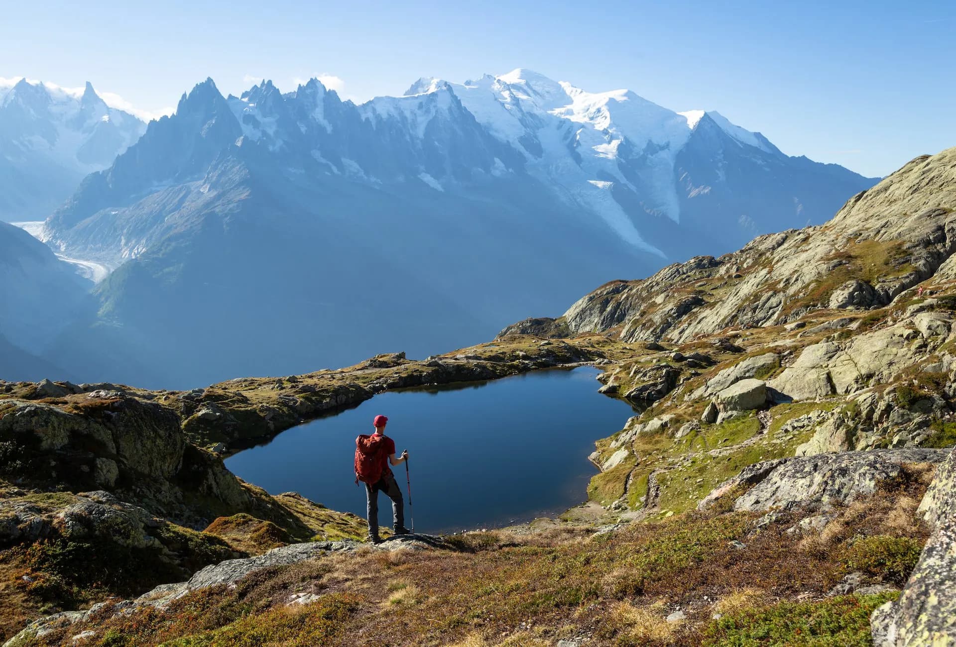 Hiker overlooking Lac de Cheserys with snow-capped alpine mountains in the background