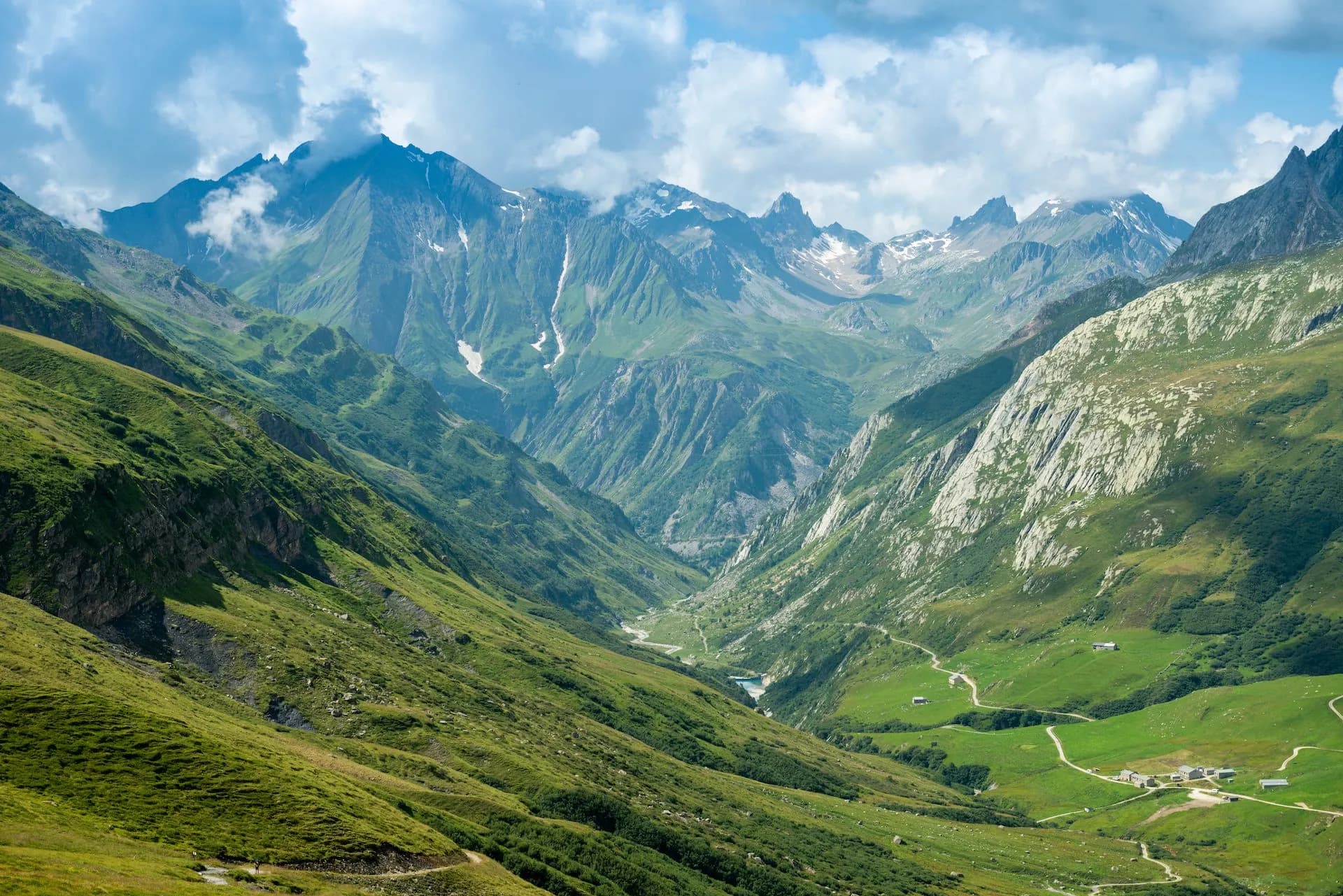 Alpine valley in Ville-des-Glaciers with steep green slopes and rocky peaks under clouds.