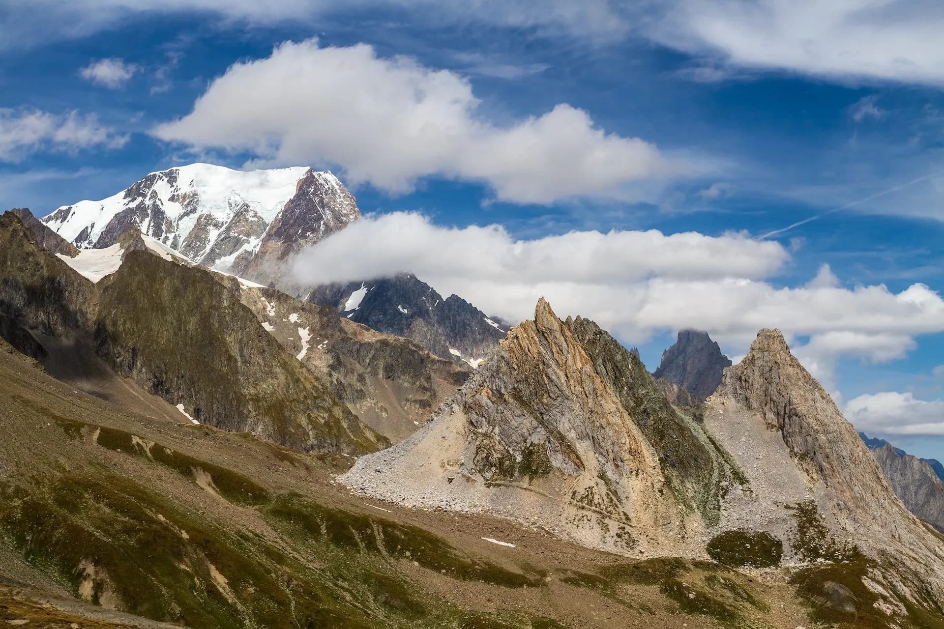 Snow-capped Mont Blanc peak above rocky slopes and sharp peaks from Col de la Seigne on the French-Italian border.
