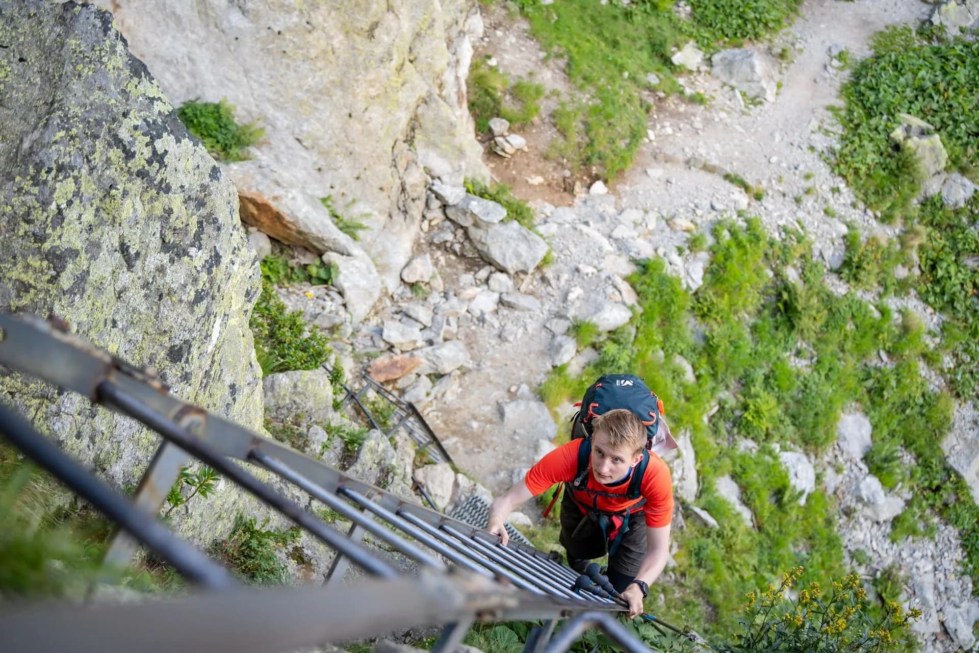 Hiker ascending metal ladder on steep rock face with green vegetation below