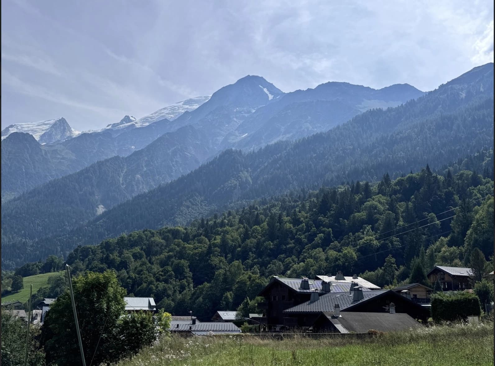 Alpine village houses below forested slopes and snow-capped mountains in Les Houches.