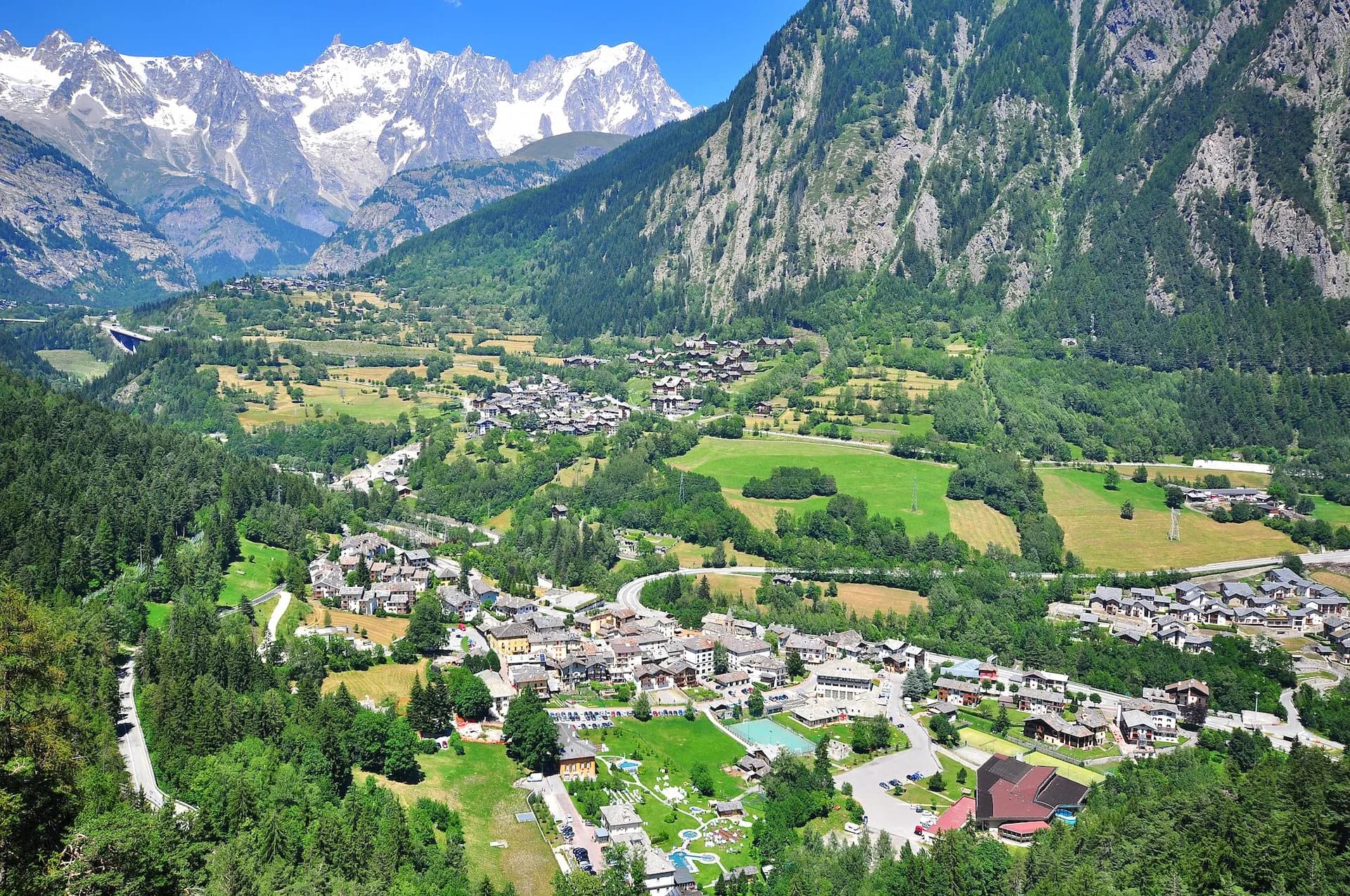 Alpine village nestled in green valley below snow-capped mountains in Courmayeur