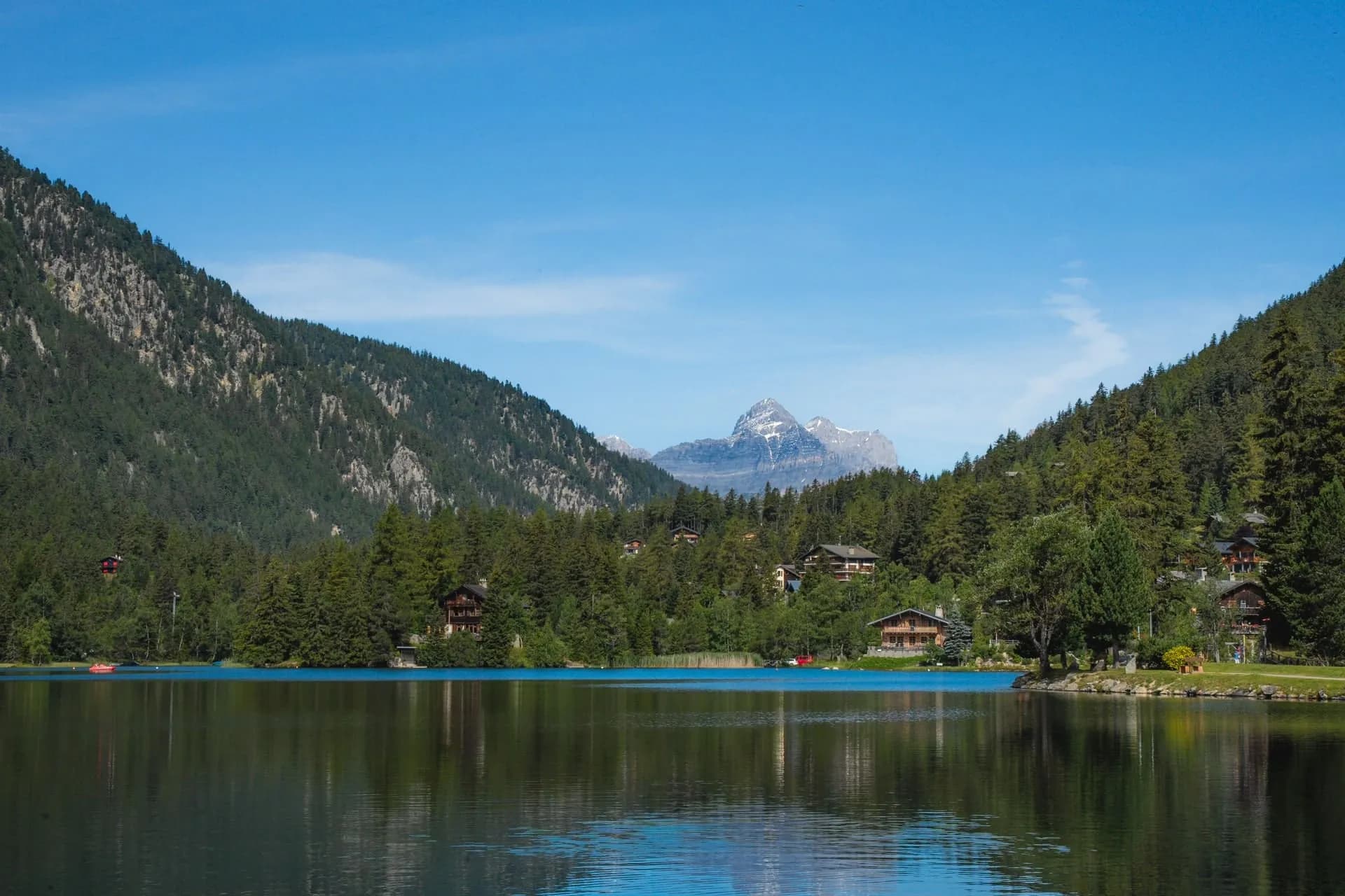 Calm lake reflecting mountains and lakeside town of Champex-Lac under a clear blue sky.