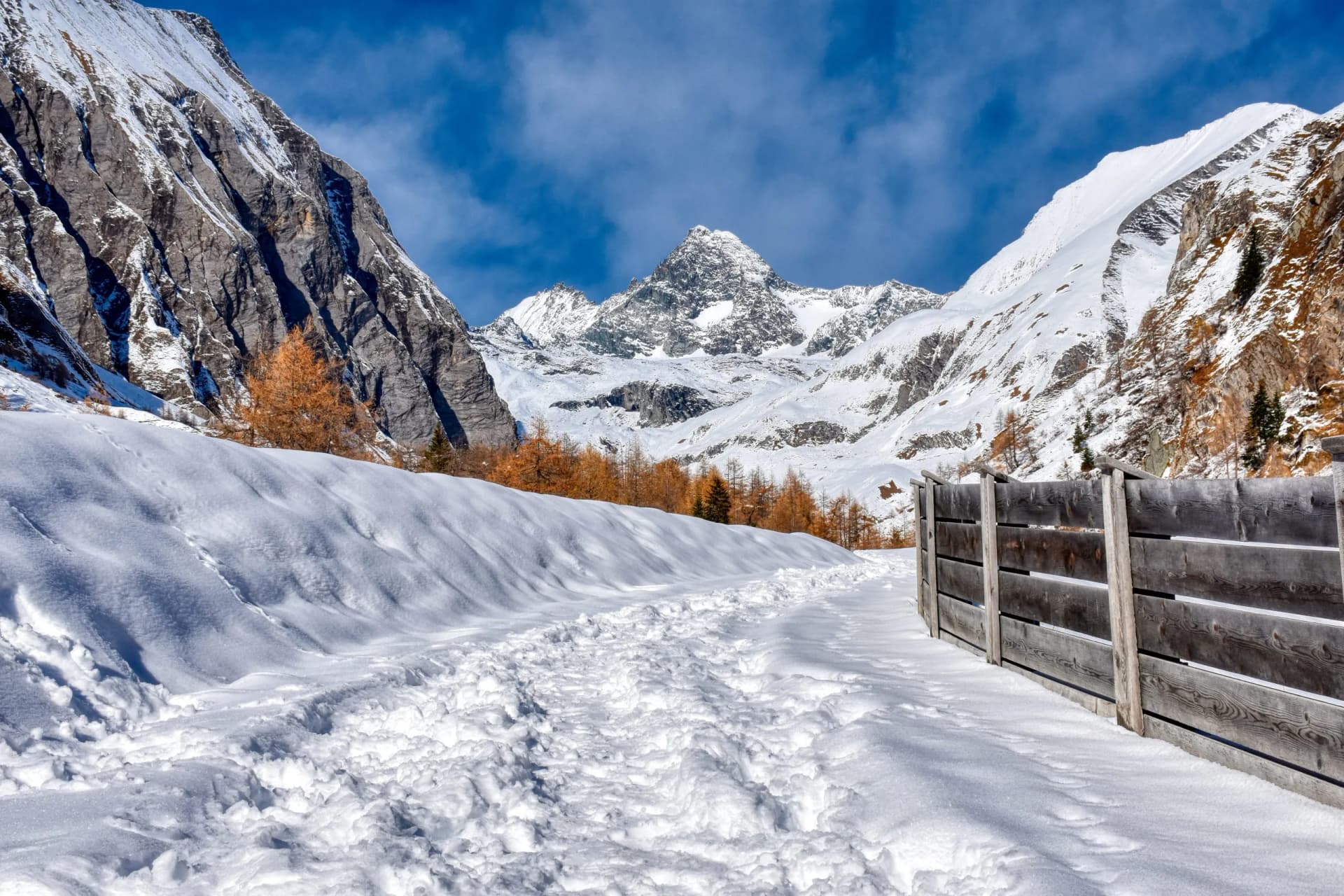 Snow-covered path leading toward snow-capped Grossglockner mountains under blue sky.