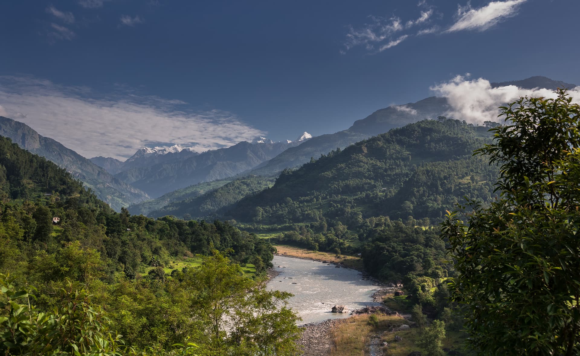 Budhi Gandaki River flowing through lush green Himalayan foothills with snow-capped peaks visible.
