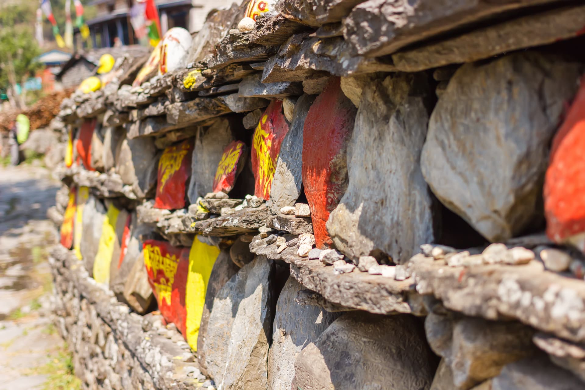 Mani wall with painted stones and prayer flags in the background at Samagaon.