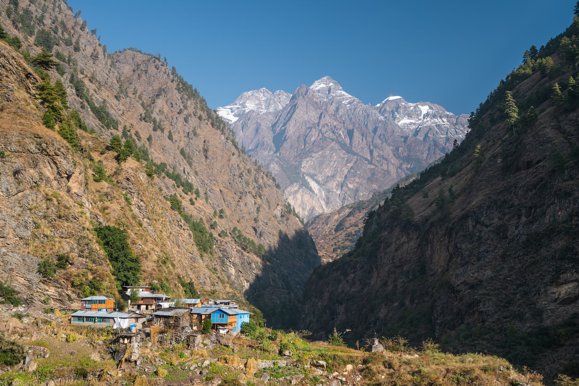 Small village nestled in a deep valley below snow-capped mountains in Manaslu region.