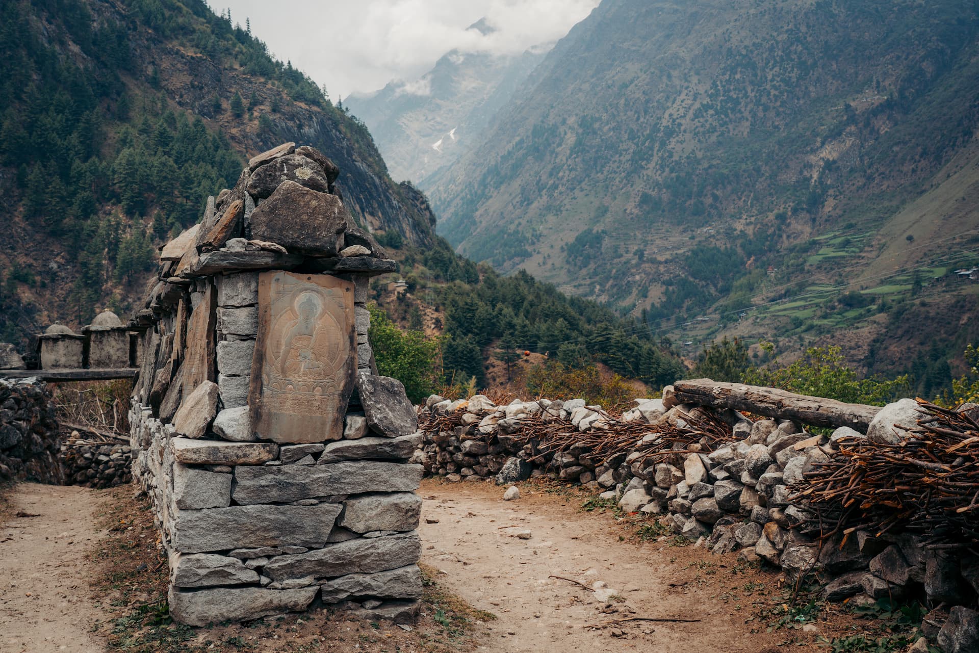 Stone mani wall with carved relief along dirt path in deep Himalayan valley on Manaslu Circuit Trek.