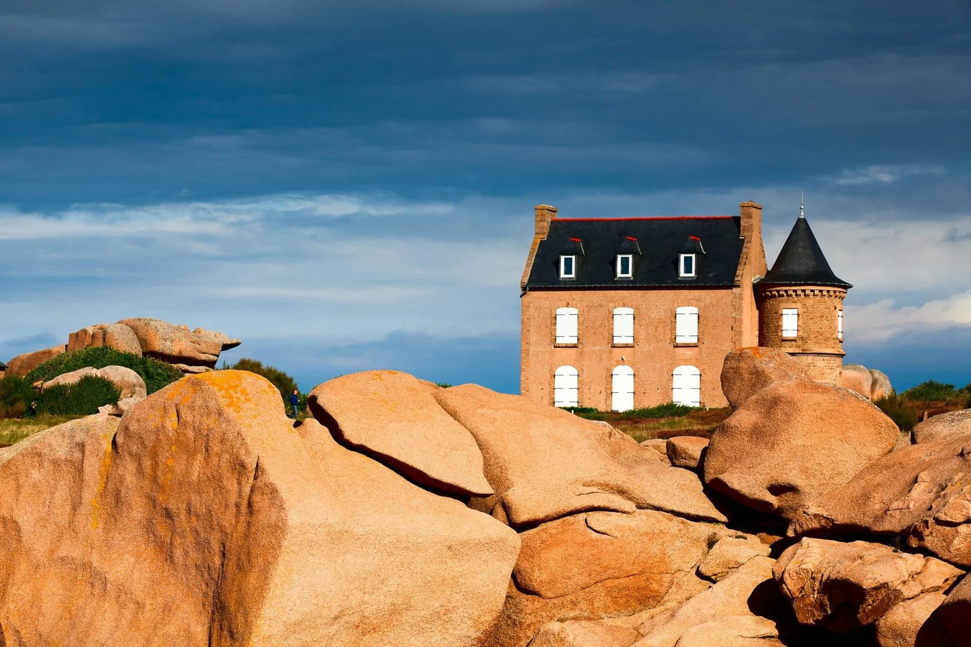Historic cottage on pink granite boulders under a dramatic blue sky, Côte de Granit Rose.