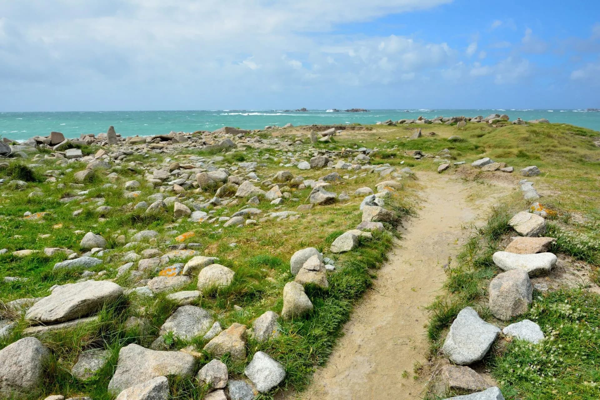 Dirt path winding through a rocky, grassy coastal area near turquoise sea near Landrellec