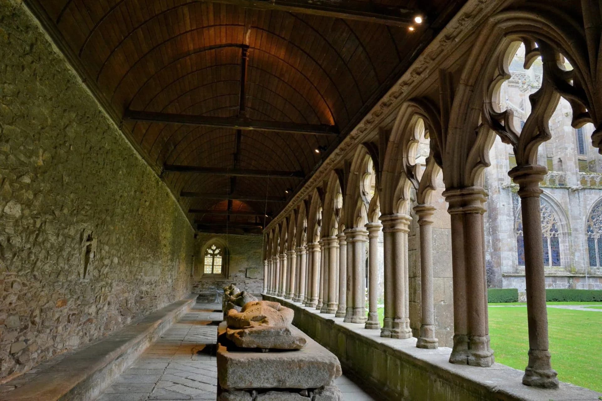 Cloister walkway with stone arches, wooden ceiling, and sarcophagi at the Tréguier Cathedral.