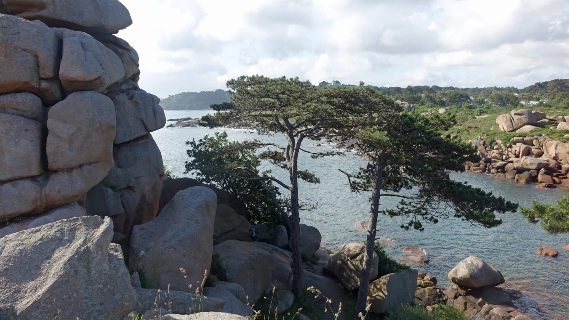 Coastal landscape near Ploumanac'h with pink granite boulders, pine trees, and blue water.
